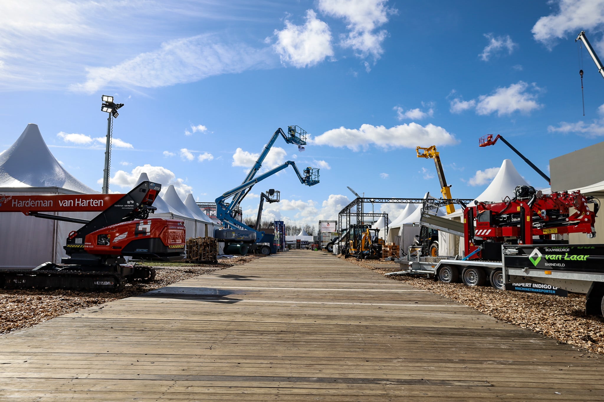 Vlonderpad tussen pagodetenten, machine transporters en hoogwerkers